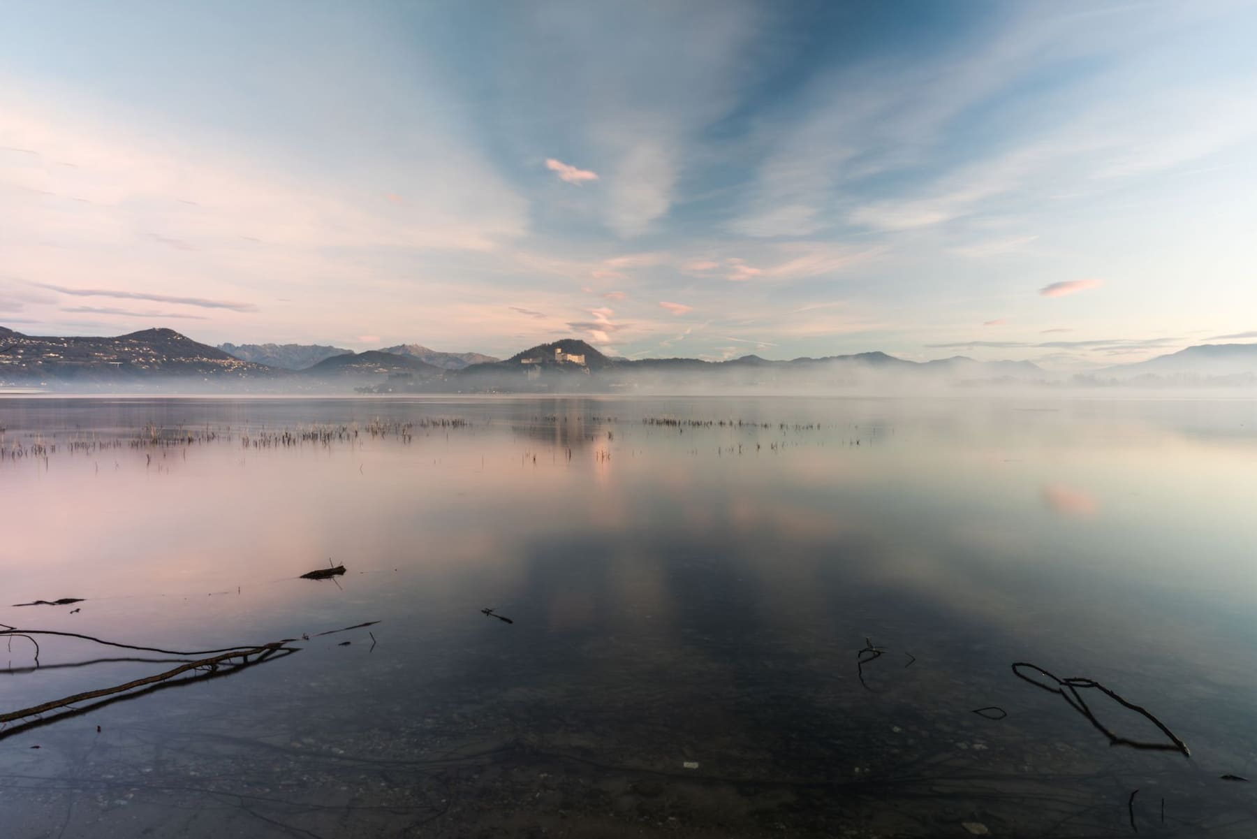Misty lake at sunrise with soft pastel sky and distant hills