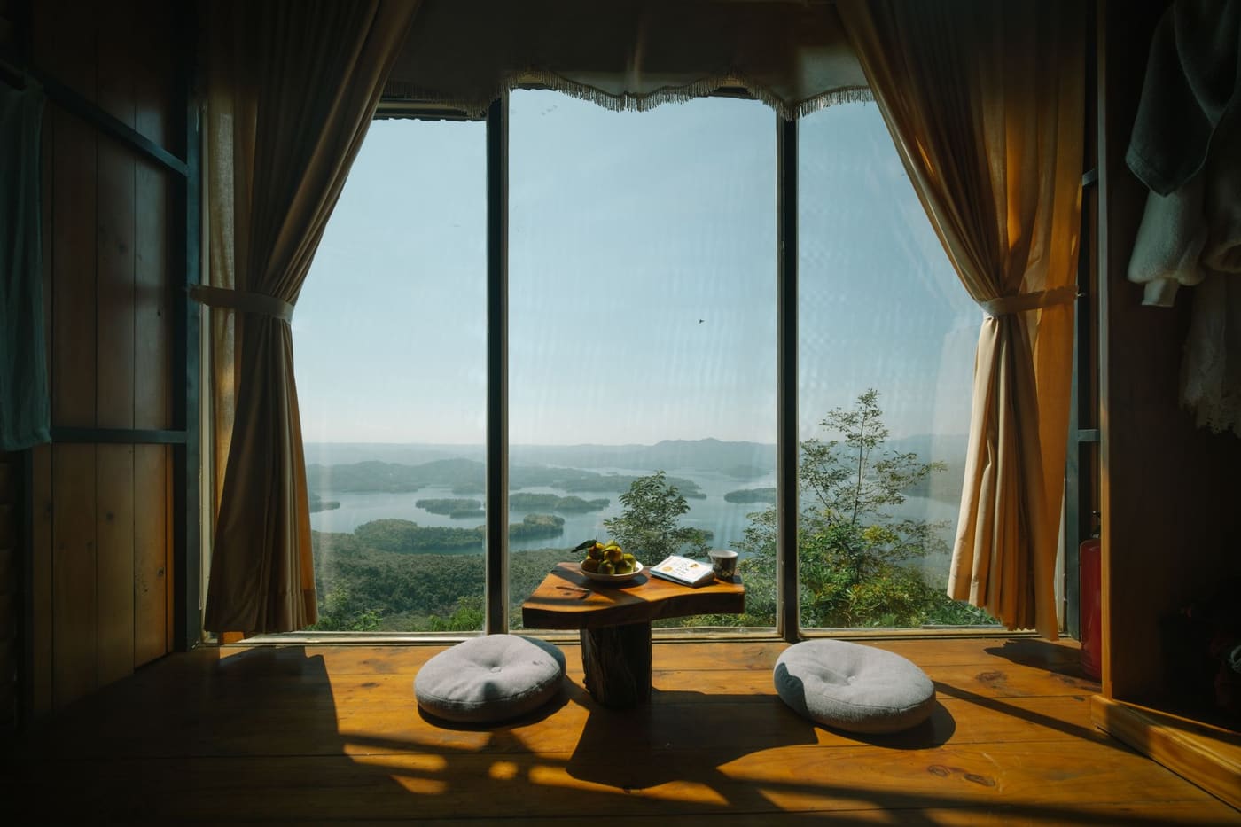 Two floor cushions and a low table beside a large window overlooking a lake and hills